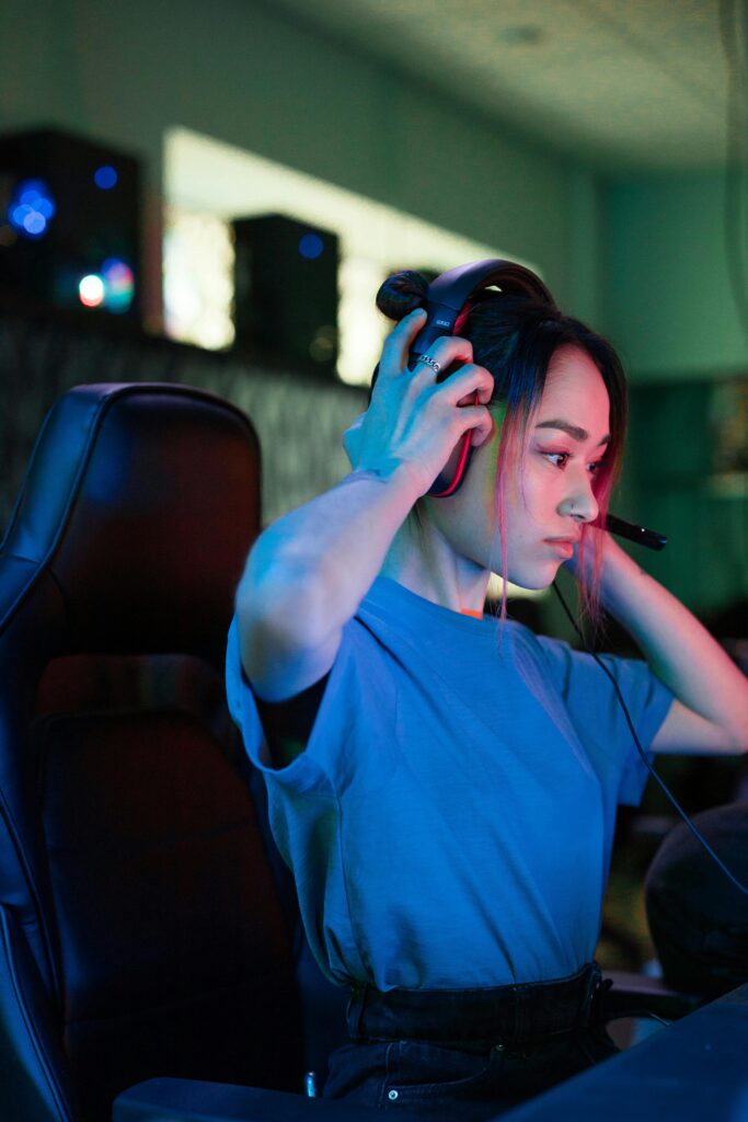 Young woman adjusting her gaming headset in a dimly lit game room, ready for an intense gaming session.